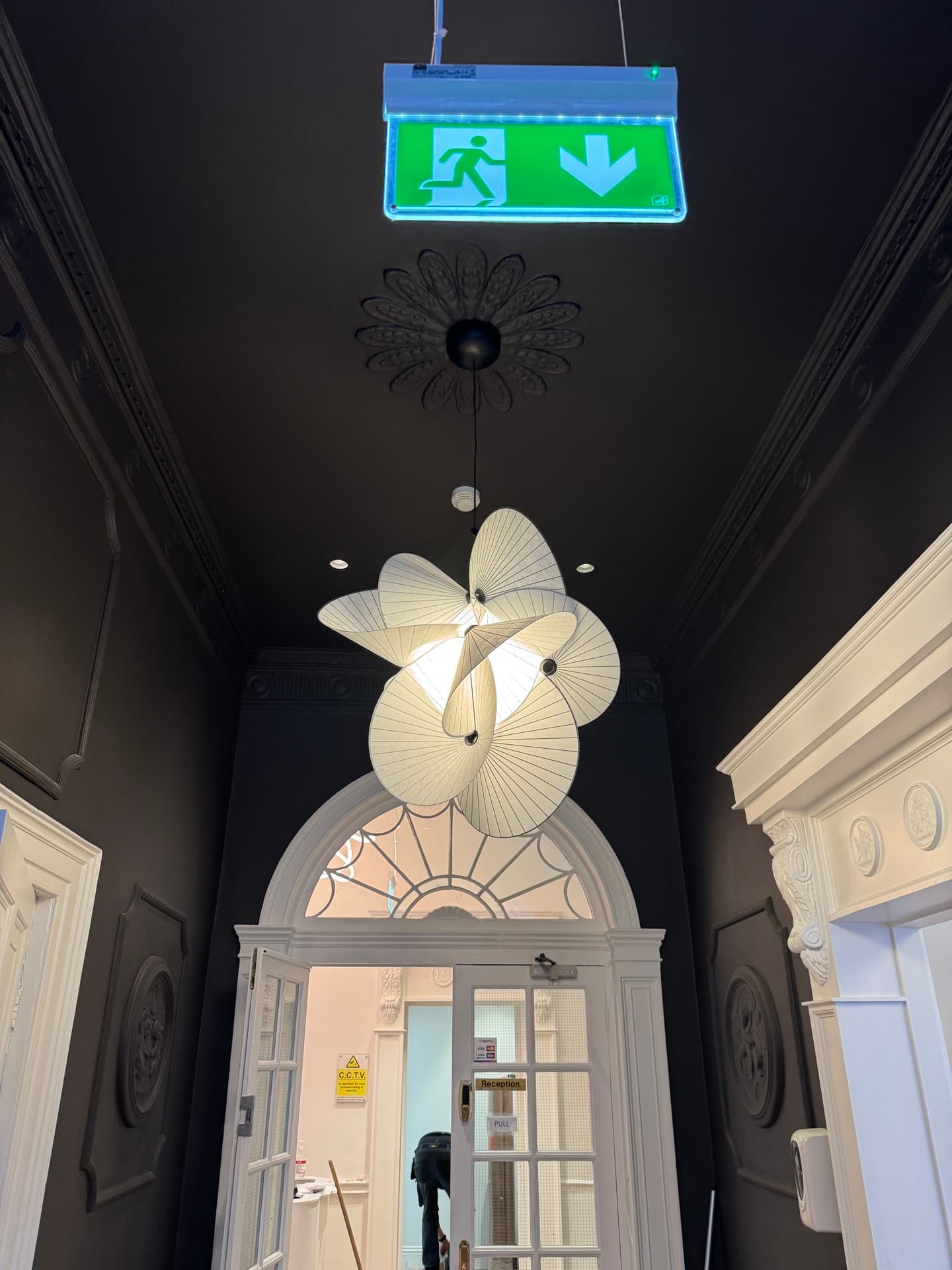 Decorative pendant chandelier with fan-shaped shades and emergency exit signage in Harcourt Dental Clinic hallway with ornate period ceiling