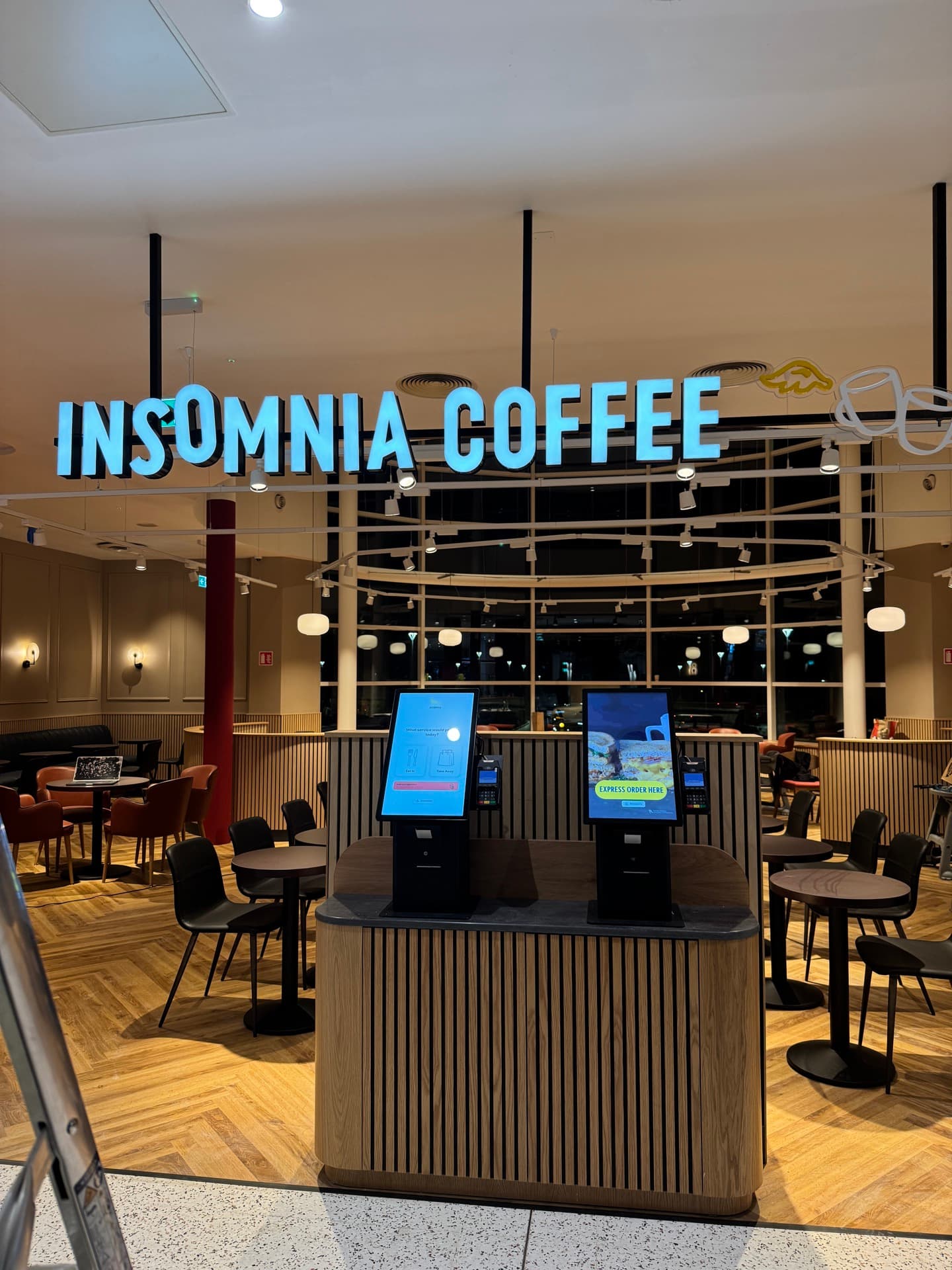 Insomnia Coffee service counter with illuminated signage, powered POS screens, and pendant lighting